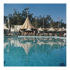 an outdoor swimming pool with umbrellas and people sitting at tables in the shade near it