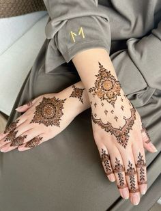 a woman's hand with henna tattoos on it and the letter m in gold