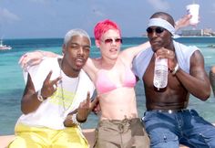 three men and a woman posing for a photo on the beach with one holding a water bottle