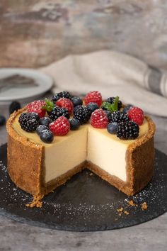 a cheesecake with berries on top is cut in half and served on a black plate