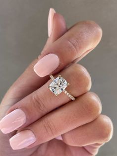 a woman's hand holding a ring with a cushion shaped diamond on it and two rows of diamonds in the middle