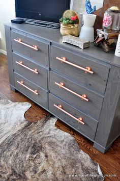 a gray dresser with pink handles on it and a cowhide rug in front of it