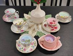 a table topped with lots of different cups and saucers next to a vase filled with flowers