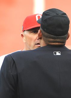 two baseball players standing next to each other on a field with one man wearing a red and white hat