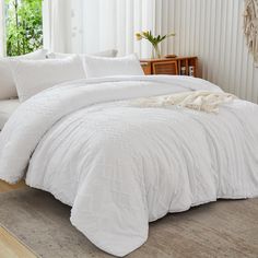 a bed with white comforter and pillows in a room next to a window on the floor