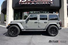 a gray jeep parked in front of a tire and wheel store with black rims