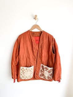 an orange jacket hanging on a white wall next to a wooden hanger with two patches