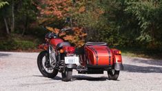 a red motorcycle parked on top of a gravel road next to trees in the background