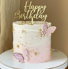 a pink and white cake with gold butterflies on it's top is sitting on a table