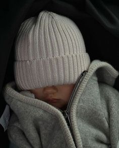 a baby in a car seat wearing a white knitted hat with zippers on it