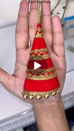 a hand holding a red and gold christmas tree ornament