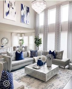 a living room filled with lots of furniture next to two windows and a chandelier