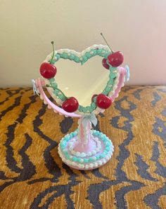 a heart shaped mirror sitting on top of a table with cherries in the middle