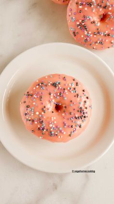 two donuts with pink icing and sprinkles on a white plate