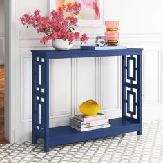 a blue console table with flowers and books on it in front of a white wall