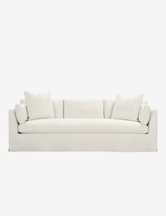 a white couch sitting on top of a white floor next to a wall with two pillows