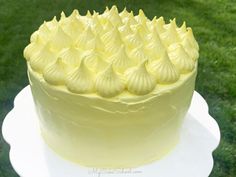 a yellow frosted cake sitting on top of a white plate with grass in the background