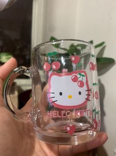 a person holding a hello kitty glass mug in their left hand with cherries on it