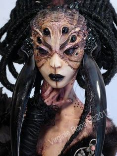 a woman with dreadlocks and makeup is wearing an elaborate mask, which has black hair