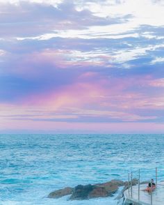 two people are sitting on a dock near the ocean as the sun sets over the water