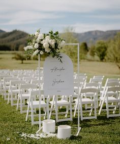 an outdoor ceremony setup with white chairs and flowers on the sign for each chair to sit in