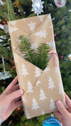 someone is holding an origami envelope in front of a christmas tree with ornaments on it