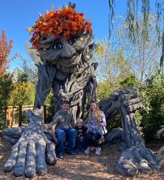 two people sitting in front of a fake tree with leaves on it's head