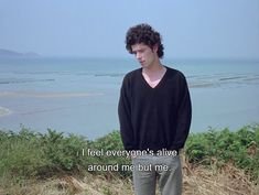 a man standing on top of a grass covered hillside next to the ocean with a quote