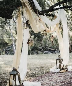 an outdoor wedding ceremony with white draping and hanging decorations on the tree branches