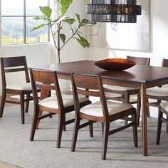 a dining room table with chairs and a bowl on it's centerpiece in front of a window