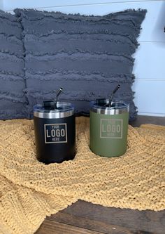 two black and green tumblers sitting next to each other on a wooden floor with a yellow blanket