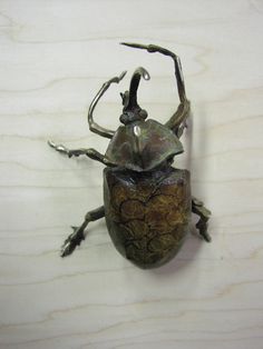 a metal bug sitting on top of a wooden table next to a white wall or floor