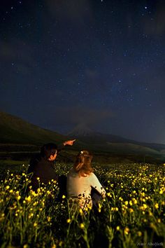 two people sitting in a field looking at the stars