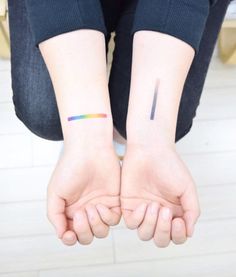 two people holding hands with tattoos on their wrist and one has a small rainbow tattoo