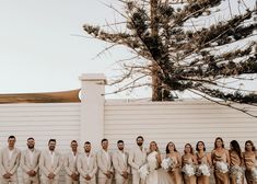 a group of people standing next to each other in front of a white wall and tree