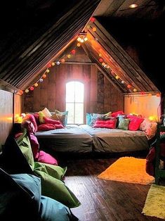 an attic bedroom with two beds and pillows on the floor in front of a window