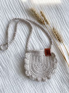 a crocheted purse sitting on top of a bed next to a dried plant