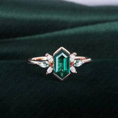 an emerald and diamond ring sitting on top of a green velvet covered surface with two white diamonds