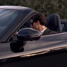 a man sitting in the driver's seat of a black car with his head out the window