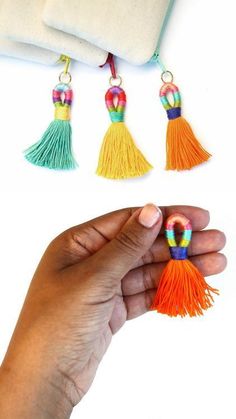 the hand is holding three different colored tassels