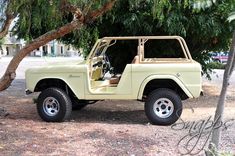 an old jeep is parked under a tree