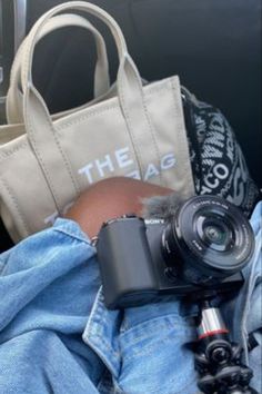 a person holding a camera in their lap with a bag on the ground behind them