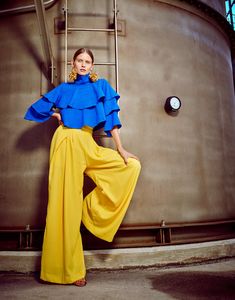 a woman in blue and yellow is leaning against a large tank with her hands on her hips