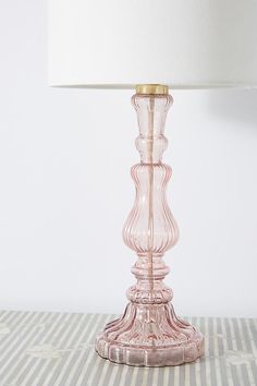 a pink glass table lamp with a white lampshade next to it on a striped surface