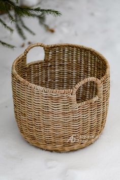 a wicker basket sitting in the snow next to a christmas tree with no leaves on it