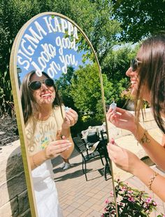 two women standing in front of a mirror with writing on it and one is brushing her teeth