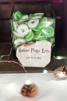 there are some green and white buttons in a glass box on the table next to pine cones