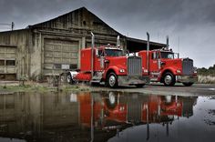 a red semi truck parked in front of an old building next to a body of water