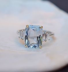 an aquamarinee and diamond ring sitting on top of a piece of white marble