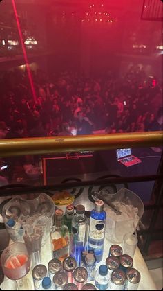 a table topped with lots of bottles and glasses next to a stage filled with people